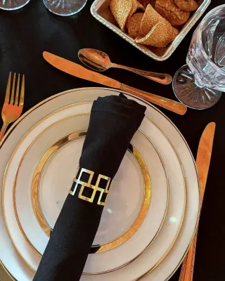 Couvert dressé sur nappe noire : assiette à filet d’or, couverts dorés et rond de serviette au monogramme de la maison